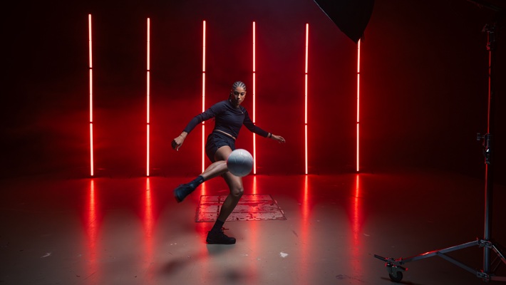 Die Fussballerin Sydney Schertenleib führt einen Trick mit einem Ball in einem dunklen Raum mit roten Lichtstreifen aus. Es handelt sich dabei um eine behind the scenes-Aufnahme für eine Werbefilmproduktion für die Uhrenmarke Norqain produziert im Mietstudio für Film- und Fotoproduktionen StudioGutenswil in der Nähe von Zürich (Schweiz).