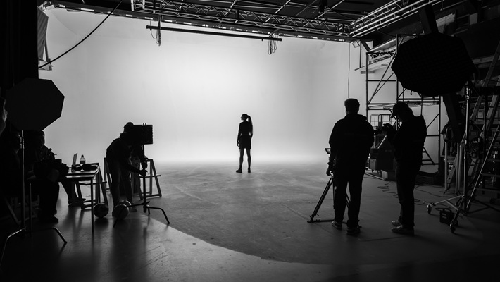 Die Fussballerin Sydney Schertenleib steht in einem Studio mit hellem Hintergrund, während mehrere Personen mit Kamera- und Lichtausrüstung arbeiten. Es handelt sich dabei um eine behind the scenes-Aufnahme für eine Werbefilmproduktion für die Uhrenmarke Norqain produziert im Mietstudio für Film- und Fotoproduktionen StudioGutenswil in der Nähe von Zürich (Schweiz).